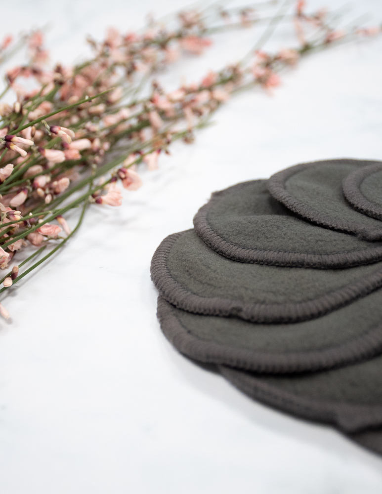Set of grey bamboo reusable make-up remover pads on marble background next to pink flowers