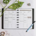 Vertical erasable monthly calendar with black pen next to assorted items on marble background