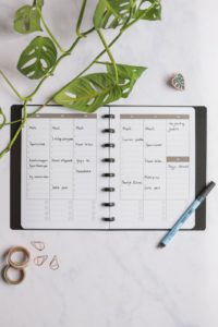 Vertical erasable monthly calendar with black pen next to assorted items on marble background